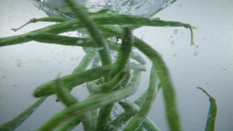 Underwater-view-of-beans-thrown-in-water-creating-a-spiral-in-clear-water,-slow-motion-effect