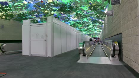 Flight-Paths-art-installation-in-Hartsfield-Jackson-International-Airport-is-visible-in-the-A-to-B-connecter-tunnel-over-temporary-construction-walls-during-airport-upgrades-with-passengers-passing