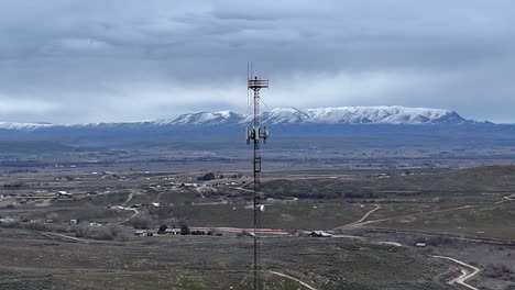 Drohne-Fliegt-Im-Orbit-Um-Einen-Sehr-Hohen-Handyturm-Im-Späten-Bewölkten-Winterabend-über-Einer-Kargen-Wüstenlandschaft