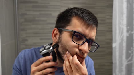 Young-man-with-glasses-using-a-shaver-for-his-beard-in-the-bathroom