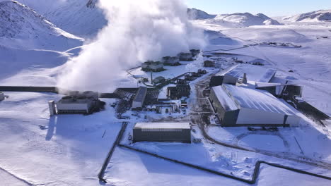 A-geothermal-power-plant-in-iceland's-snowy-landscape,-steam-rising,-aerial-view