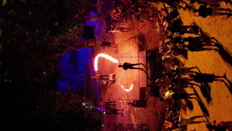 Tourists-at-Thai-beach-bar-jumping-fire-rope,-VERTICAL