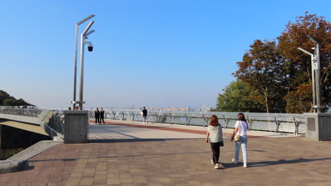 People-walking-on-the-famous-Glass-Bridge-in-Kyiv-city-center-Ukraine,-sunny-weather-and-blue-sky,-bridge-with-glass-floor-panels,-4K-shot