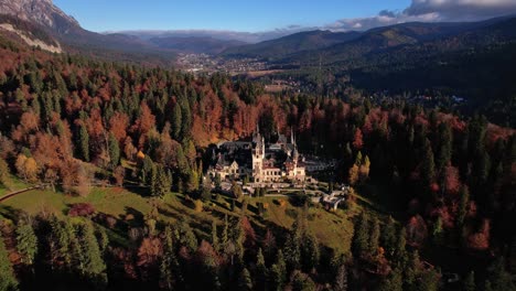 Autumn-colors-envelop-Peles-Castle-in-a-tranquil-mountain-setting,-aerial-view