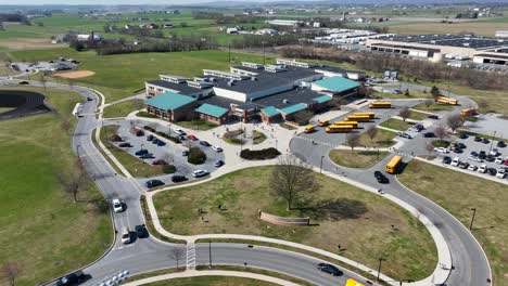 Drone-flight-over-american-school-with-parking-yellow-buses-and-traffic-on-roundabout