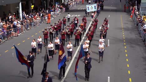 Eine-Blaskapelle-Marschiert-Die-Straße-Entlang-Und-Wird-Am-Anzac-Day-Von-Den-Menschenmassen-Angefeuert,-Die-Sich-An-Den-Straßenrändern-Ansammeln.