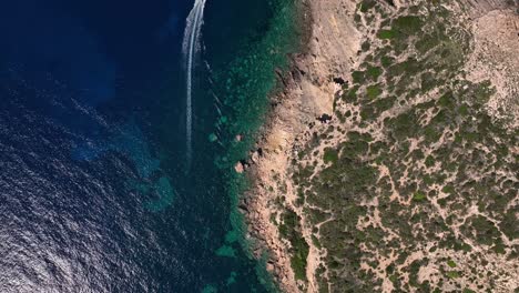 Boat-driving-along-cliffs-over-crystal-clear-water-top-down-drone-shot