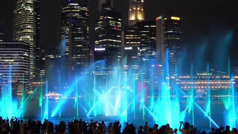 Magical-evening-with-spectacular-visual-effect,-SPECTRA-light-and-water-show-against-downtown-cityscape-in-the-background,-timel-apse-shot-capturing-massive-crowds-at-the-Marina-Bay-Sands-event-plaza