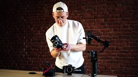 Filmmaker-at-indoor-studio-near-red-brick-wall-change-camera-lens-on-table