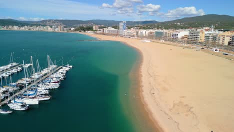 Desde-El-Cielo,-Palamós-Se-Despliega-Como-Un-Pintoresco-Tapiz-De-Playas-De-Arena,-Calas-Rocosas-Y-Laderas-De-Color-Verde-Esmeralda.