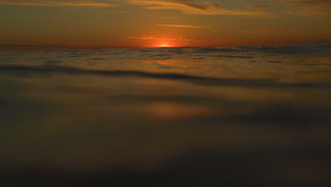 Red-setting-sun-ball-drops-low-on-horizon-as-ocean-water-waves-rise-and-fall-with-tide