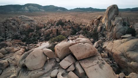 Ein-Mann-Steht-Auf-Einer-Schroffen-Felsformation,-Während-Eine-Drohne-Ihn-Mitten-Im-Joshua-Tree-Nationalpark-Umkreist