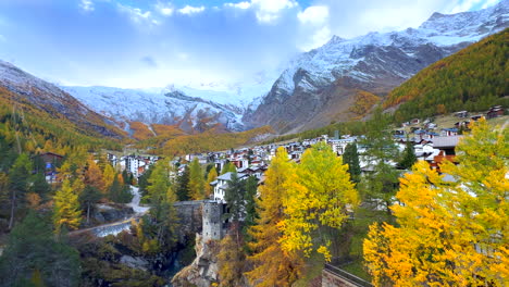 Early-moody-morning-Saas-Fee-Zermatt-Saastal-Swiss-alps-mountain-peaks-shaded-alpine-valley-chalet-ski-resort-town-Switzerland-downtown-river-crossway-bridge-vibrant-yellow-larks-slow-pan-to-the-left