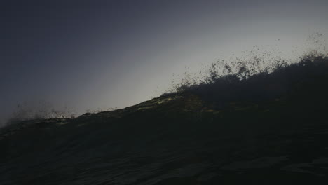 Frontal-view-of-wave-breaking-and-crashing-down-spreading-mist-and-green-sunset-light-across-water