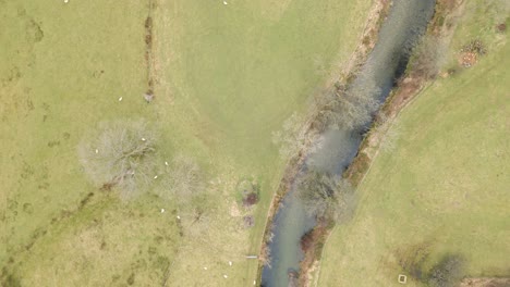Orbiting-overhead-drone-shot-of-a-scenic-meadow-and-a-river-flowing-through-it,-located-in-Grasmere-a-mountain-village-in-Cumbria-in-Northwest-England,-in-United-Kingdom