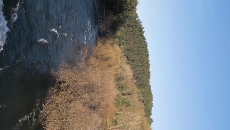 Dynamic-River-Flow-Between-Lush-Banks---aerial-vertical-video