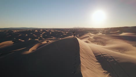 Un-Dron-Volando-En-El-Desierto-Alrededor-De-Un-Hombre-Parado-Sobre-Las-Dunas