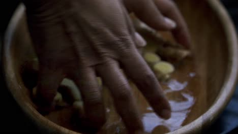 Picking-up-freshly-cut-ginger-from-a-bowl-of-water-to-add-it-to-a-blender-making-a-beverage