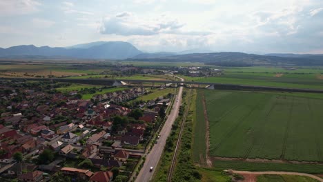 Rasnov-city-with-lush-fields,-rolling-hills,-and-houses-in-daylight,-aerial-view