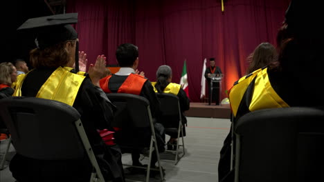 Graduating-Class-of-2023-clapping-hands-after-a-speech-is-given-to-them-at-a-Mexican-University-with-gowns-in-different-colors