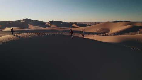 Cuatro-Hombres-Caminando-En-El-Desierto-Sobre-Las-Dunas-Al-Amanecer,-Hora-Dorada