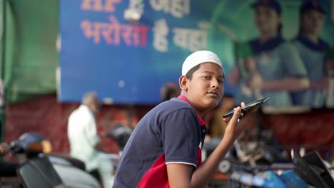 Toma-Cinematográfica-De-Un-Niño-Hablando-Por-Teléfono-Frente-A-La-Cámara-Y-Sonriendo,-Gente-India