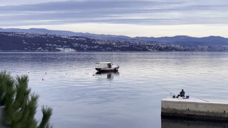 Fisherman-on-peer-Boat-parked-on-Sea-shore-with-town-in-distance-close-up,-Opatija,-Croatia