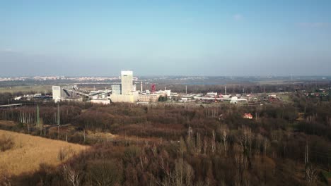 Industrial-complex-of-the-Darkov-coal-mine-surrounded-by-wooded-area,-the-town-visible-in-the-background-under-a-clear-sky