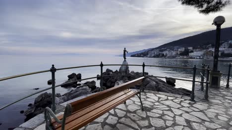 Statue-of-a-woman-on-sea-shore-bench-Resort-town-island-in-distance-approached-Lovran,-Opatija,-Croatia