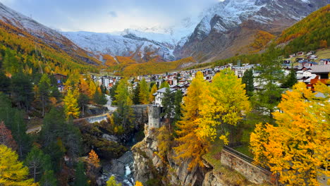 Early-moody-morning-Saas-Fee-Zermatt-Saastal-Swiss-alps-mountain-peaks-shaded-alpine-valley-chalet-ski-resort-town-Switzerland-downtown-river-crossway-bridge-vibrant-yellow-larks-slow-pan-reveal-up