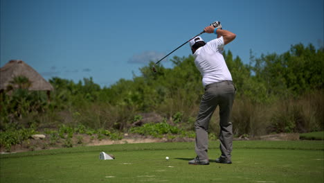 Zeitlupe-Eines-Mexikanischen-Lateinamerikanischen-Golfers-In-Adidas-Outfit,-Der-An-Einem-Sonnigen-Tag-Mit-Einem-Schwingenden-Eisen-Den-Ball-Hart-Schlägt