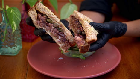 Slow-motion-of-a-person-wearing-black-latex-gloves-holding-and-presenting-a-prosciutto-with-fig-sauce-and-capers-sandwich