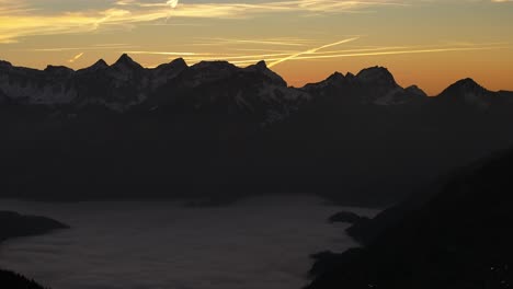 Drone-flies-over-mountains-in-the-valley-are-fogy-clouds-and-in-the-distance-high-mountains-with-snow-in-Amden,-Weesen,-Glarus,-Switzerland,-sunrise-mood