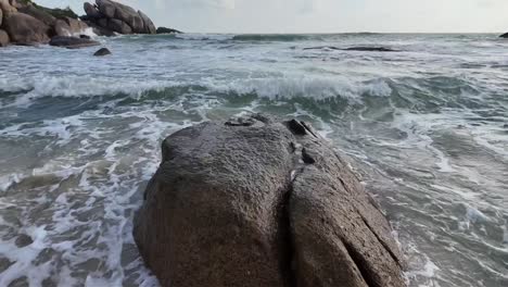 Slow-motion-shot-of-sea-waves-crashing-against-smooth-stone-on-beach