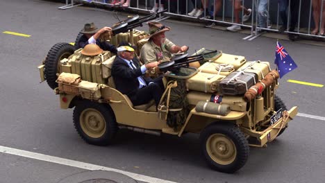 Veterans-riding-on-armoured-fighting-vehicle,-Willys-Jeep-attached-with-machine-guns-driving-down-the-street,-participating-in-the-annual-Anzac-Day-parade