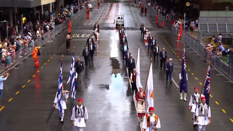 People-holding-Greek-and-Australian-flags-marching-down-the-street,-participating-the-annual-tradition-Anzac-Day-parade,-two-countries-fought-alongside-during-the-war,-commemorating-those-who-served