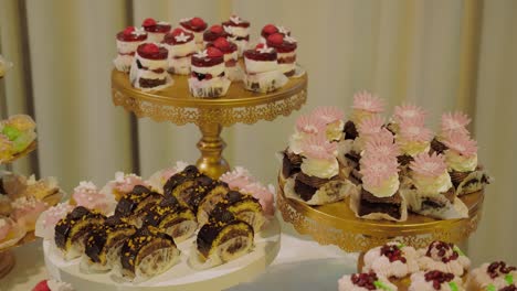 Close-up-shot-with-gold-cake-stands-filled-with-multiple-cupcakes-strawberries-chocolate-rolls,-tracking-shot