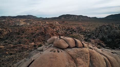 A-lonely-man-standing-on-a-rugged-rock-formation-while-a-drone-flying-backward