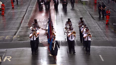 Music-band-perform-and-march-down-Adelaide-street-with-crowds-gathered-alongside,-honouring-the-memory-of-Anzac-Day-veterans