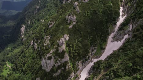 A-serpentine-river-cutting-through-the-dense-greenery-of-bucegi-mountains,-aerial-view