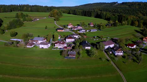 Pequeño-Y-Pintoresco-Pueblo-Enclavado-En-Un-Valle-Verde-Y-Exuberante,-Con-Un-Río-Sinuoso-Que-Serpentea-Por-El-Centro-Y-Casas-Con-Tejados-Rojos-Arracimadas-A-Lo-Largo-De-Sus-Orillas.