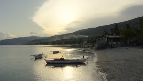 Tropischer-Strand-Auf-Der-Insel-Cebu-Mit-Fischerbooten-Und-Rauch-In-Den-Hügeln-Bei-Sonnenuntergang