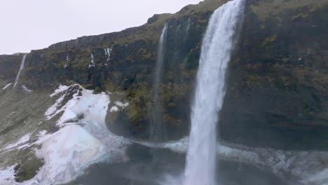 Aerial-rising-shot-of-Seljalandsfoss-waterfall-in-Iceland,-snowing,-wintertime