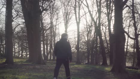 A-wooded-forest-with-a-man-walking-up-and-down-the-rugged-path-on-a-bright-cold-winter-afternoon-in-Richmond-Park,-United-Kingdom