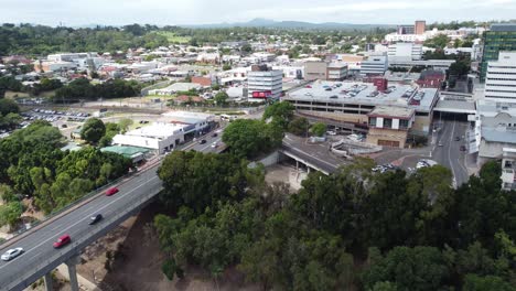 Vista-Aérea-De-Un-Pequeño-Centro-De-La-Ciudad-Dando-Marcha-Atrás-Sobre-Un-Río-Marrón-Y-Un-Puente