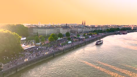 Orilla-Del-Río-Garona-Durante-La-Feria-Del-Vino-Llena-De-Multitudes-Al-Atardecer,-Toma-Aérea-De-Aproximación