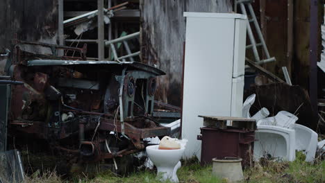 Dead-engine,-abandoned-fridge,-toilet-and-other-trash-outside-with-grass-around,-handheld