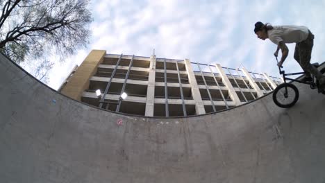 BMX-rider-wall-riding-skatepark-bowl-sideways-in-extreme-800fps-slow-motion,-static-wide-symmetrical-fisheye-in-4k