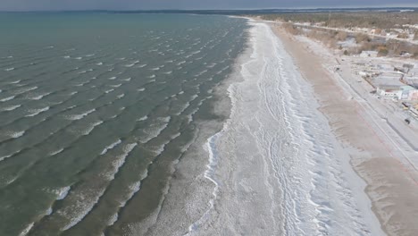 Eine-Sanfte-Küstenlinie-Mit-Rhythmischen-Wellen,-Strandgemeinde-Sichtbar,-Ruhige-Atmosphäre,-Luftaufnahme
