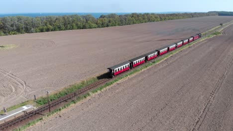 Luftaufnahme:-Schmalspurbahn-Mit-Dampfantrieb-Auf-Dem-Land,-Vorbei-An-Feldern-Und-Mit-Dem-Meer-Im-Hintergrund